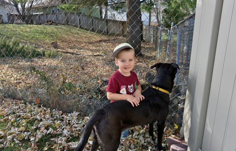 Kid smiling next to a black dog