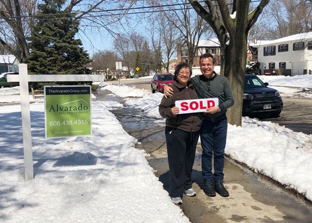 woman smilnig with agent outside in the snow with a sold sign