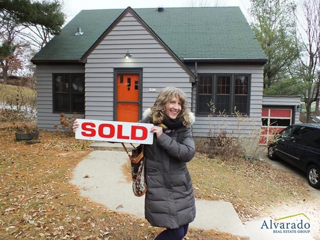 woman outside of a house holding a sold sign