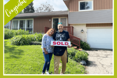 couple smiling outside of a house holding a sold sign