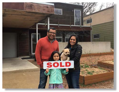 A family smiling with a sold sign in front of a house